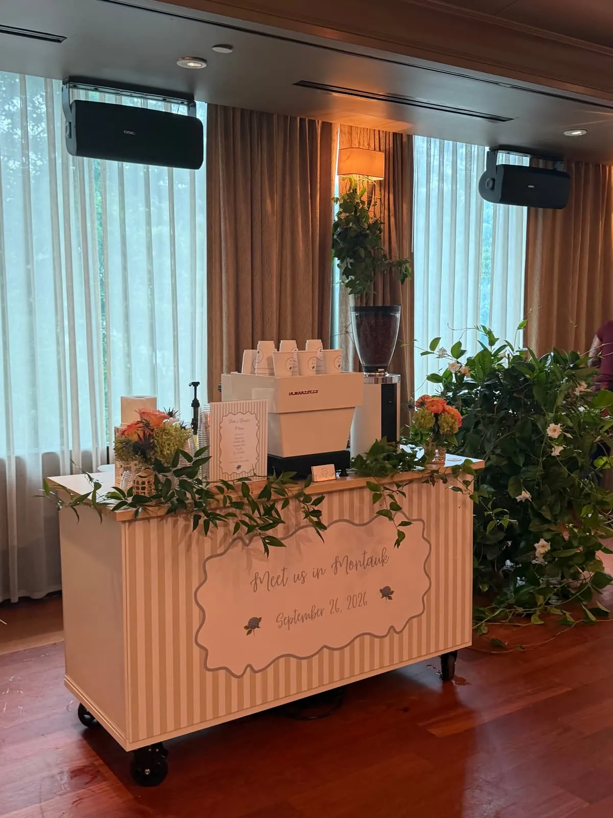 Peach striped coffee cart with an espresso machine, menu and fresh flowers at an indoor celebration
