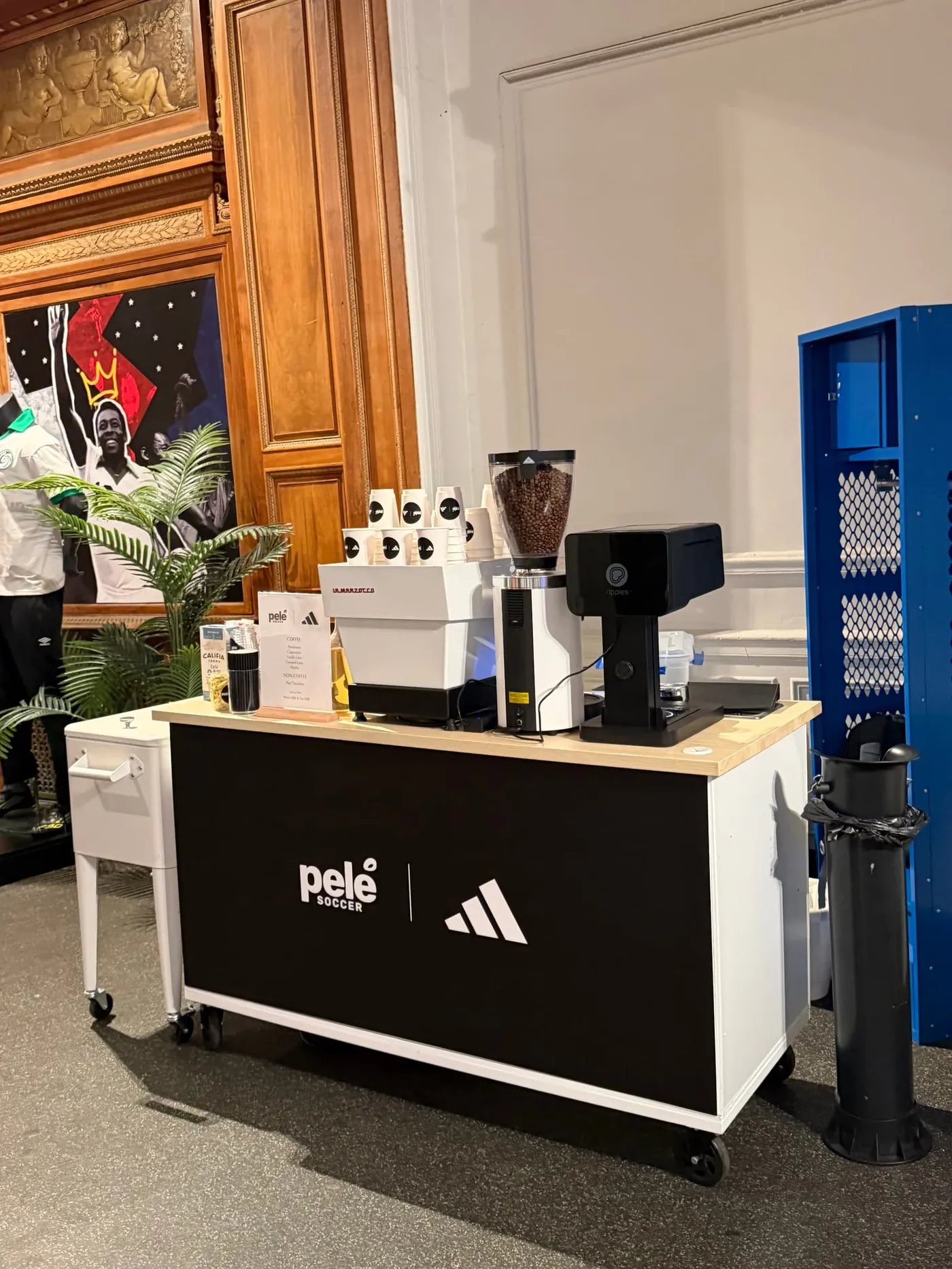 Black espresso cart wrapped with Pelé Soccer and adidas logos in a historic NYC building