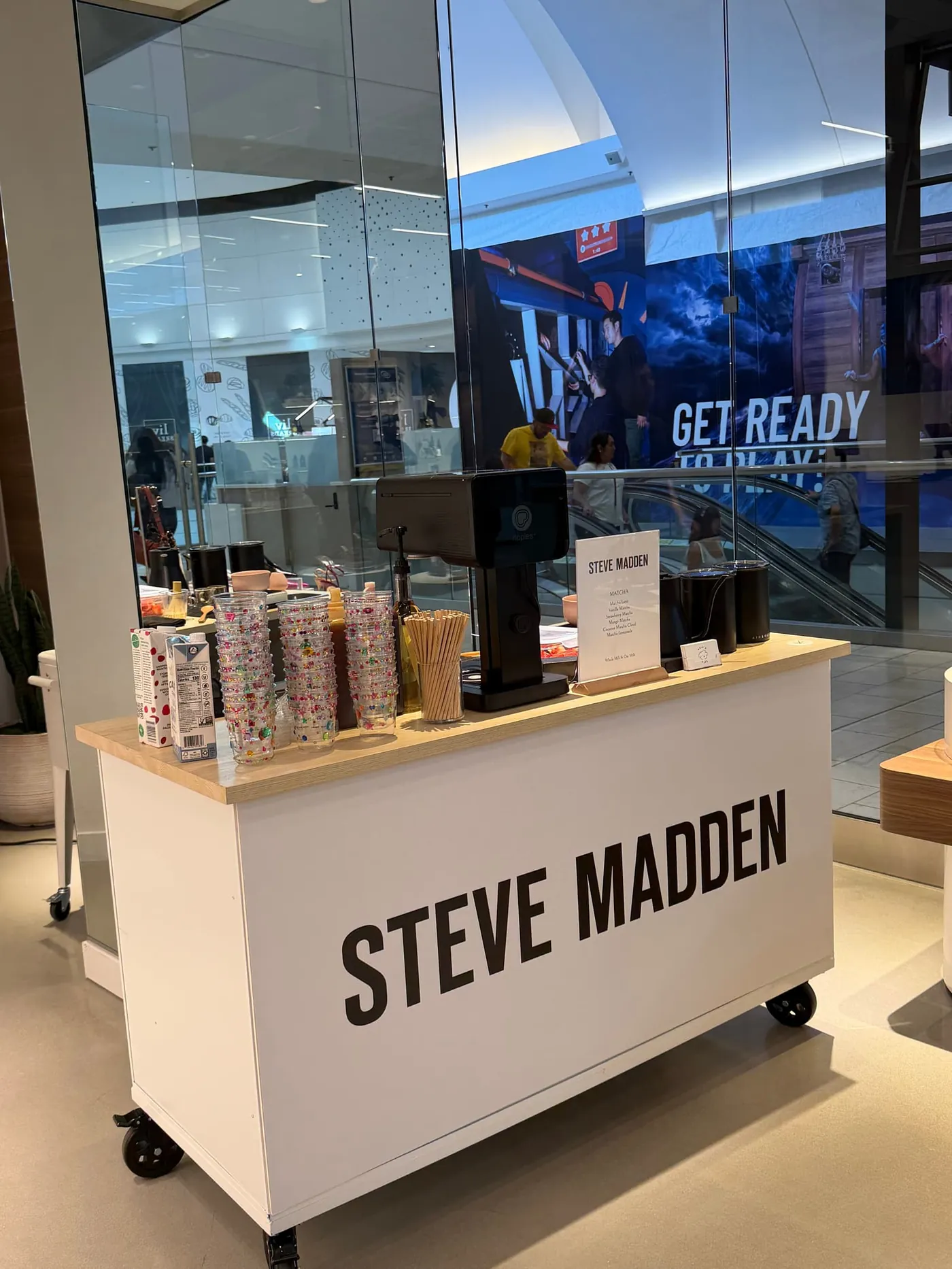 White coffee cart wrapped with the Steve Madden logo inside a shopping center